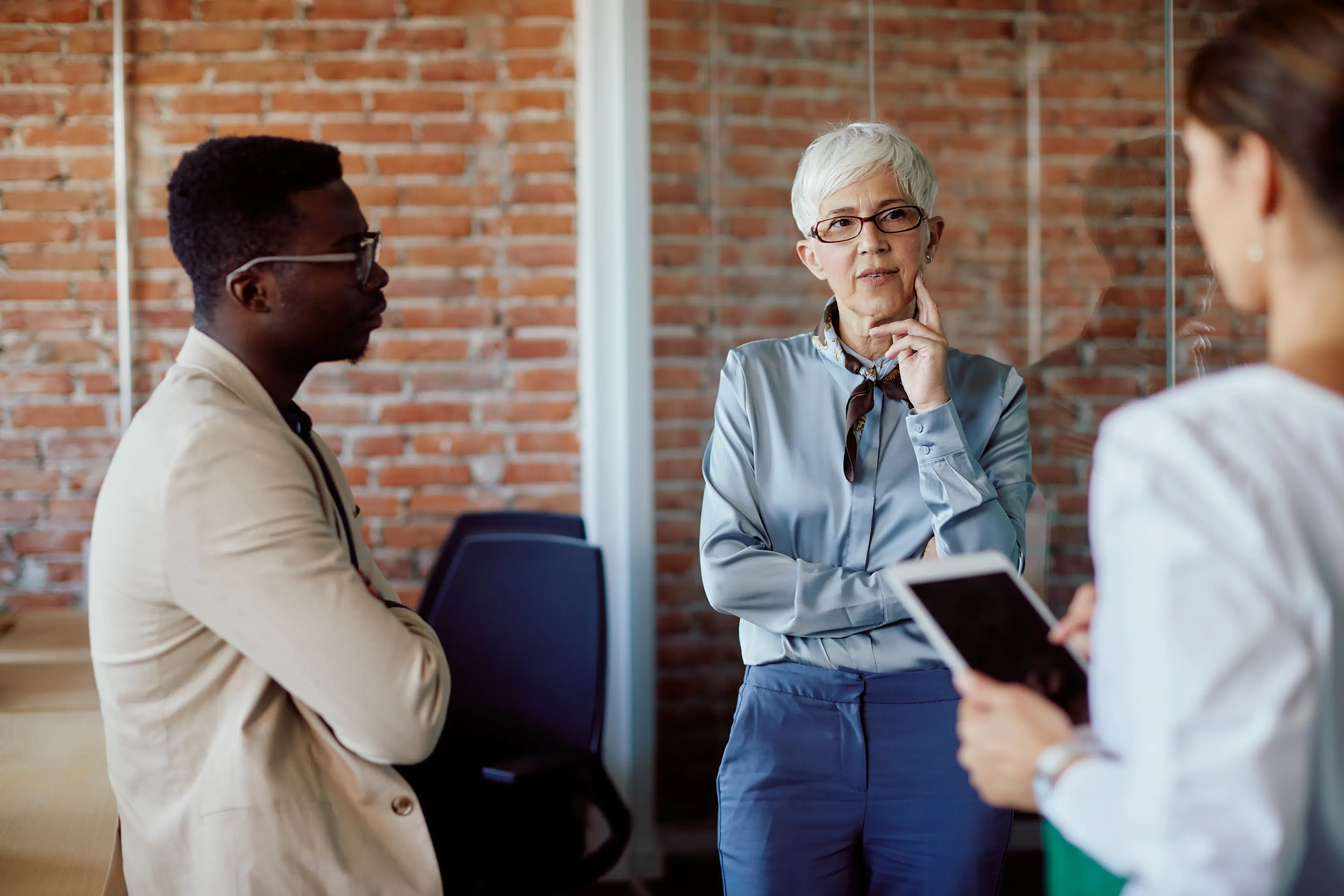 Three colleagues in conversation in a brick-walled office