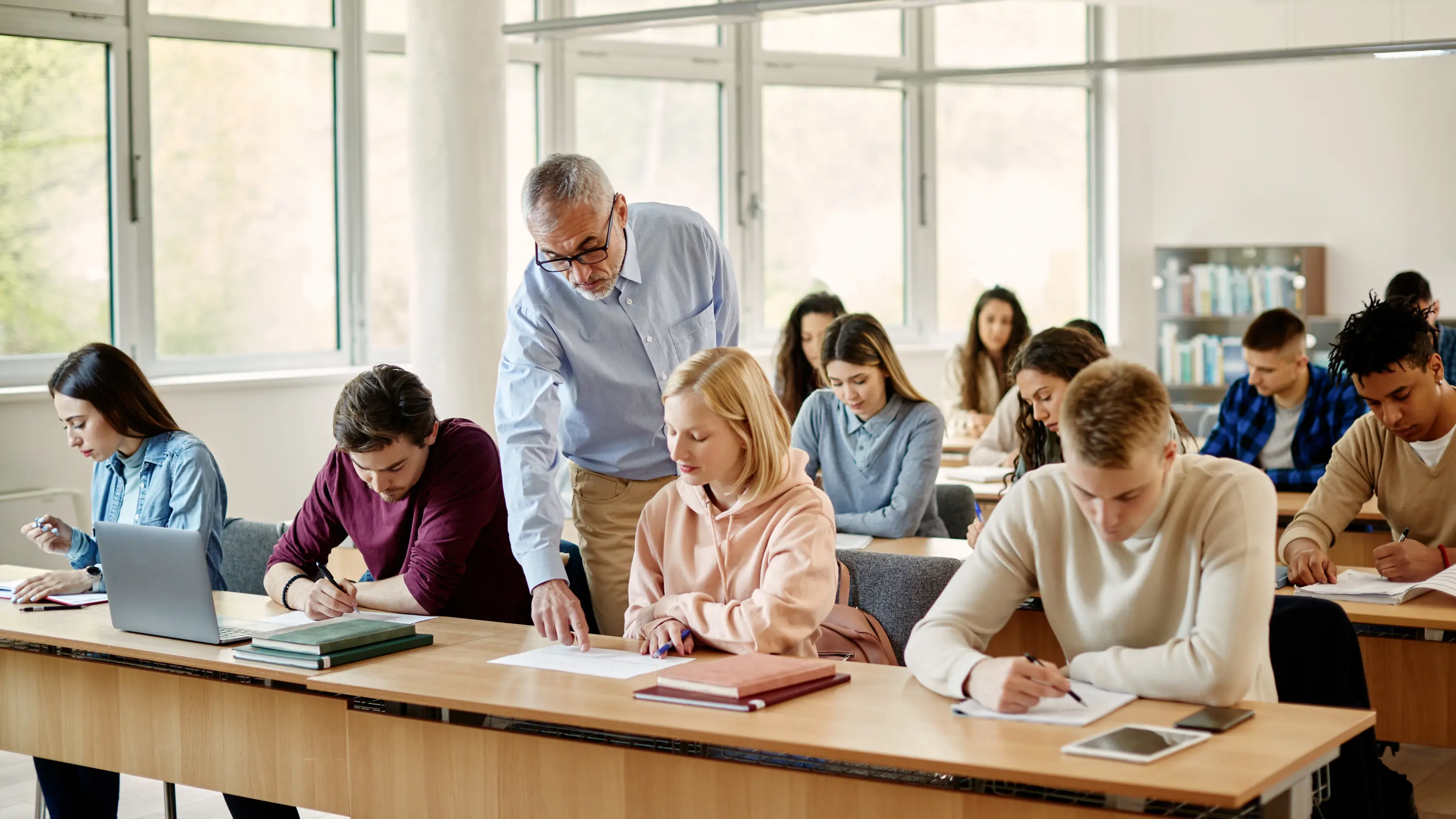 Students at work in a bright classroom while a teacher checks in