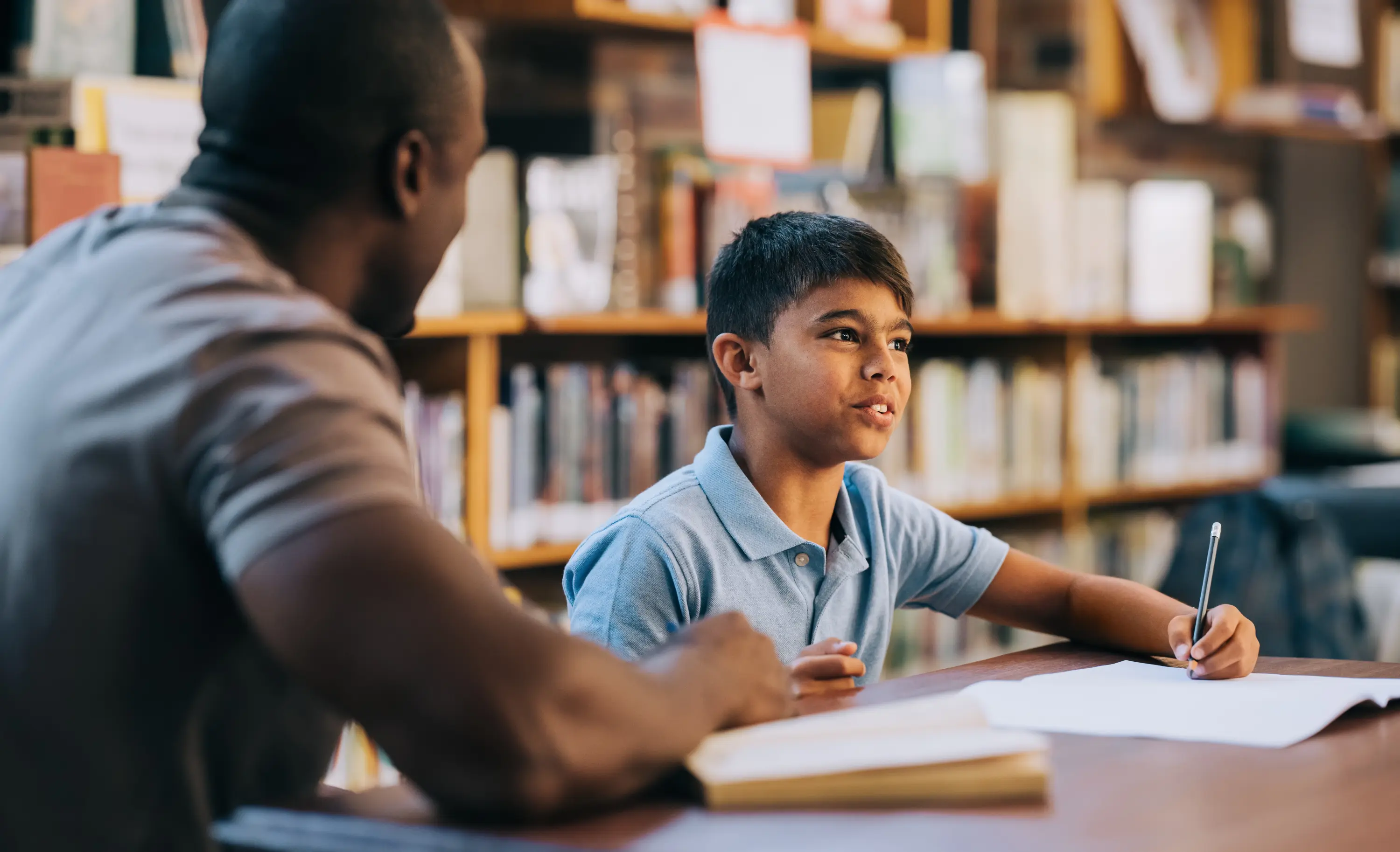 A mentor working through a lesson with a young learner in a library